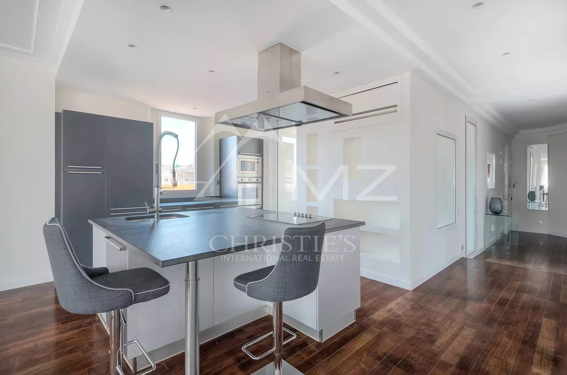 Modern kitchen with a large island, gray bar stools, and stainless steel appliances in a bright, open space.