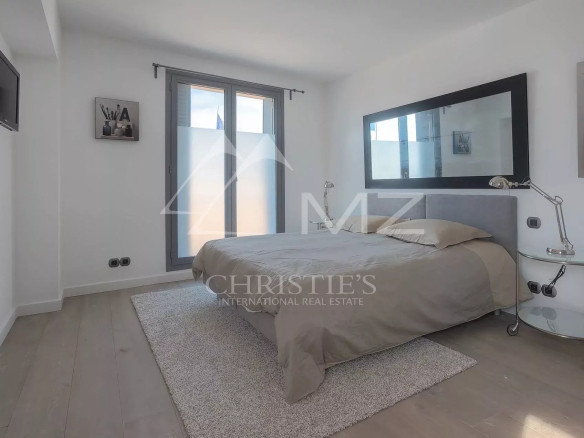 Bright minimalist bedroom with a gray upholstered bed, large black-framed mirror, and glass side table lamp on the right.