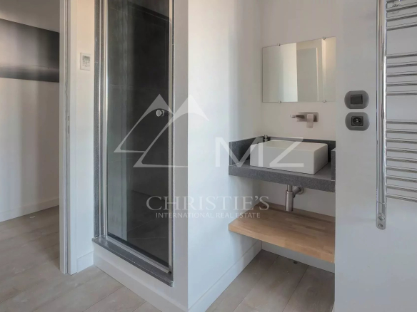 Modern bathroom with wall-mounted rectangular sink on a gray countertop, a wood shelf beneath, a mirror above, and a chrome towel warmer on the right; glass shower enclosure on the left.