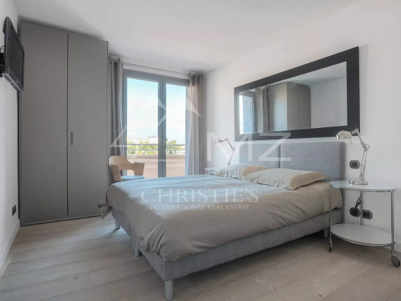 Modern bedroom with a gray upholstered bed, mirrored headboard, chrome bedside tables, a large framed mirror, and a wardrobe near a sliding balcony door.