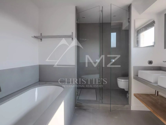 Modern bathroom with a built-in tub on the left, a glass shower in the center, and a white rectangular sink on a light gray counter on the right; grey tiles throughout.