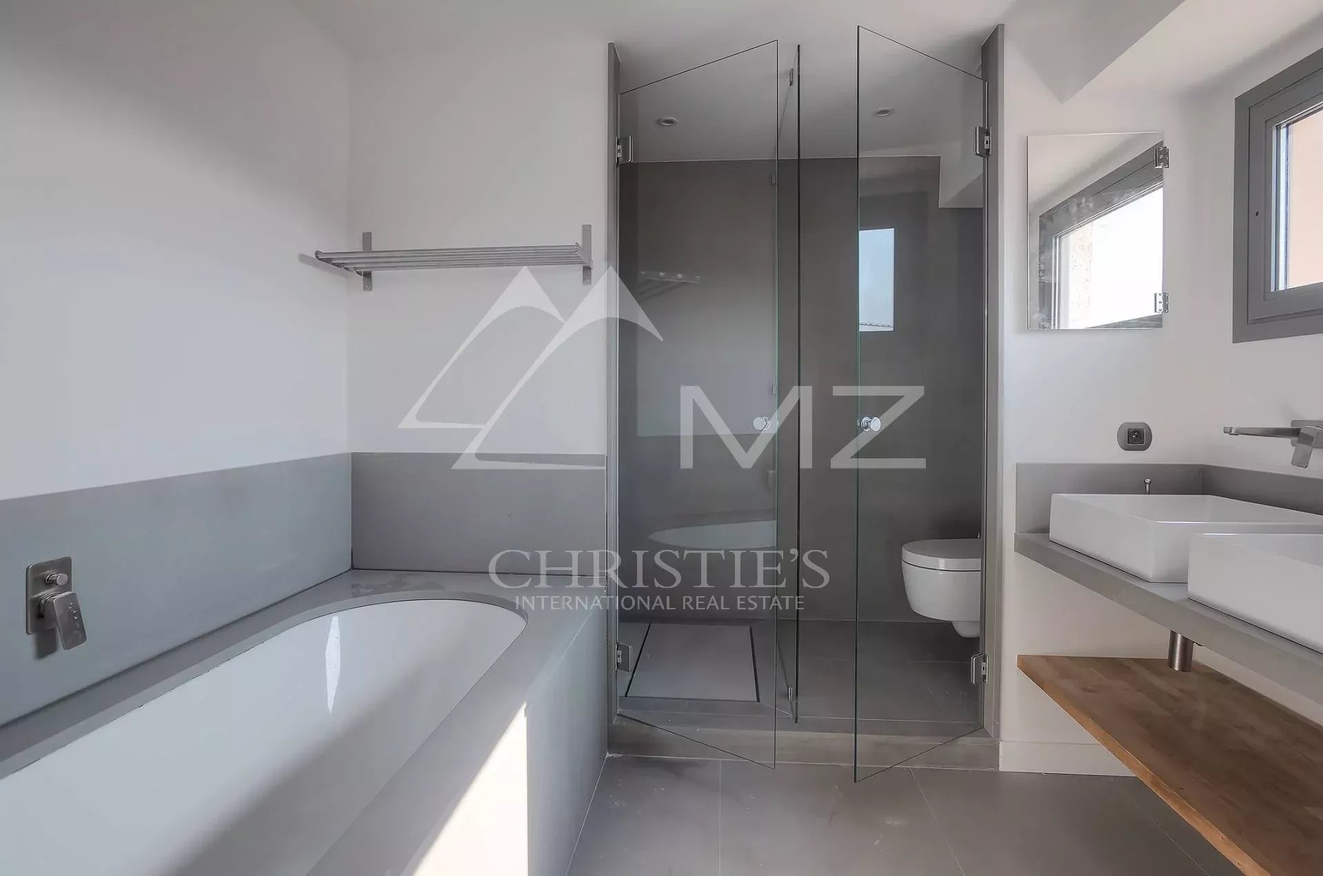 Modern bathroom with a built-in tub on the left, a glass shower in the center, and a white rectangular sink on a light gray counter on the right; grey tiles throughout.
