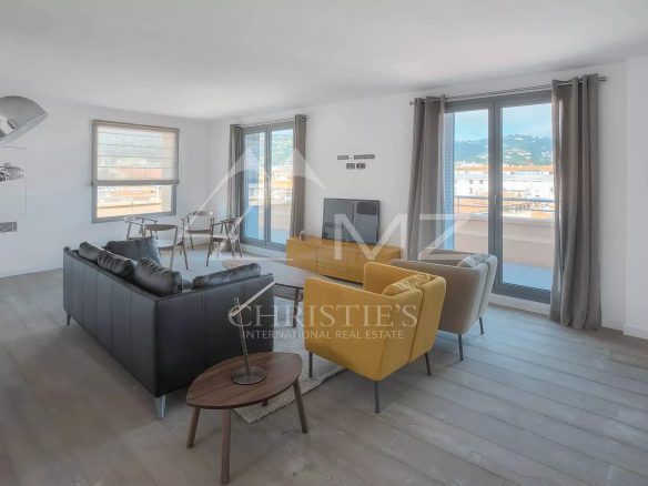 Spacious modern living room with a dark leather sofa, two mustard yellow chairs, a wooden coffee table, and a TV on a low console; large glass doors to a balcony and city views.