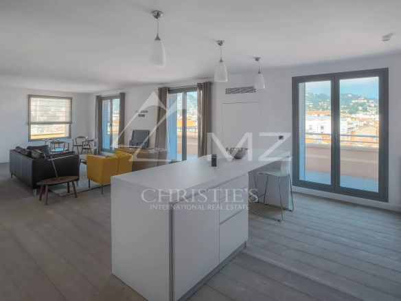 Open-plan living area with a white kitchen island, a yellow chair, and a gray sofa facing large windows and a balcony with a city view.