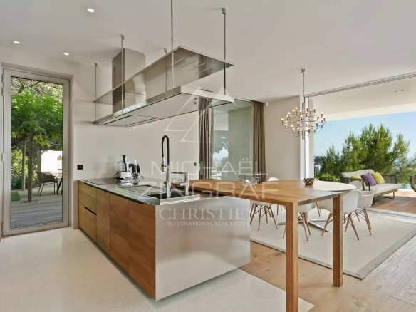 Cuisine moderne avec îlot central et salle à manger, ouverte sur l'extérieur.