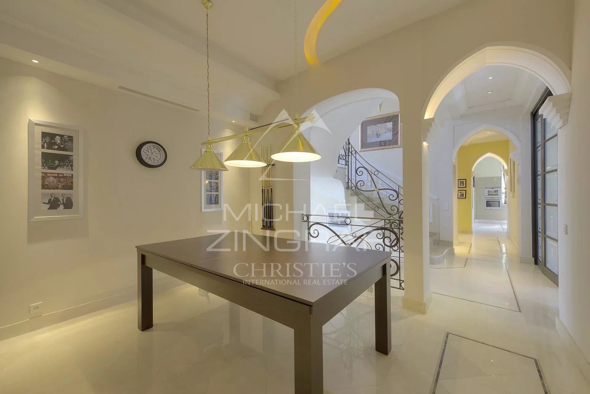 Intérieur d’un hôtel particulier à Cannes Intérieur d'un hôtel particulier à Cannes avec une table, des luminaires et un escalier décoratif.