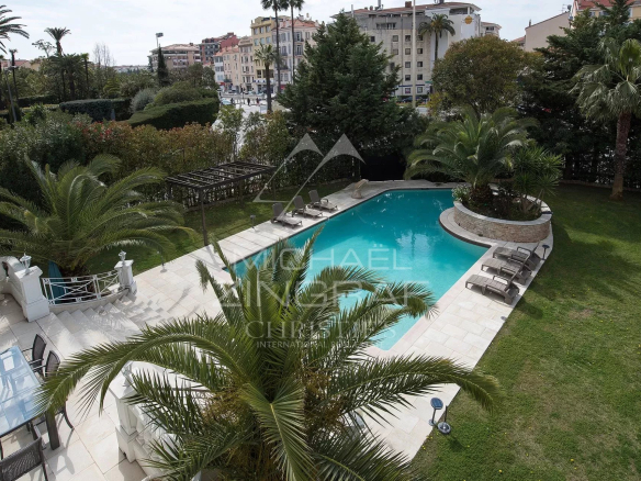 Vue d'ensemble d'une piscine entourée de palmiers et d'un jardin dans un hôtel particulier à Cannes.
