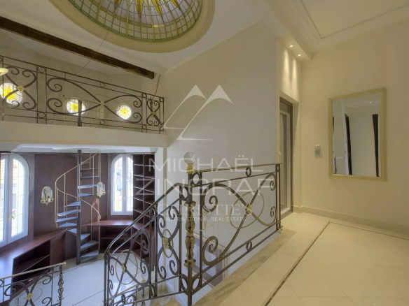 Intérieur d'un hôtel particulier à Cannes avec un escalier en fer forgé et des fenêtres décoratives.