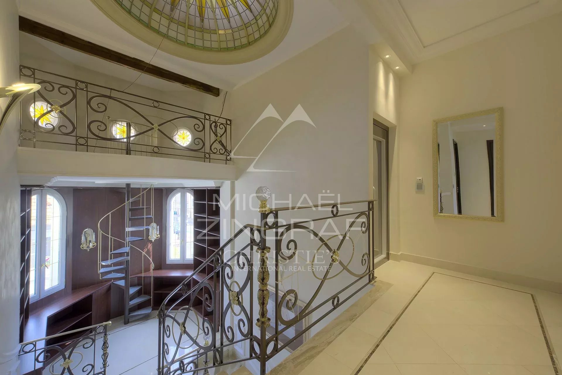 Intérieur d’un hôtel particulier à Cannes Intérieur d'un hôtel particulier à Cannes avec un escalier en fer forgé et des fenêtres décoratives.
