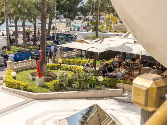 Restaurant terrace on the Croisette in Cannes with views of the sea and palm trees.