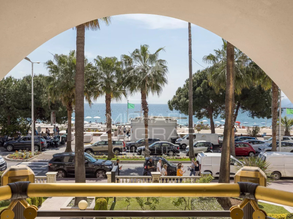 Panoramic sea view from an apartment on the Croisette in Cannes, with palm trees and cars below.