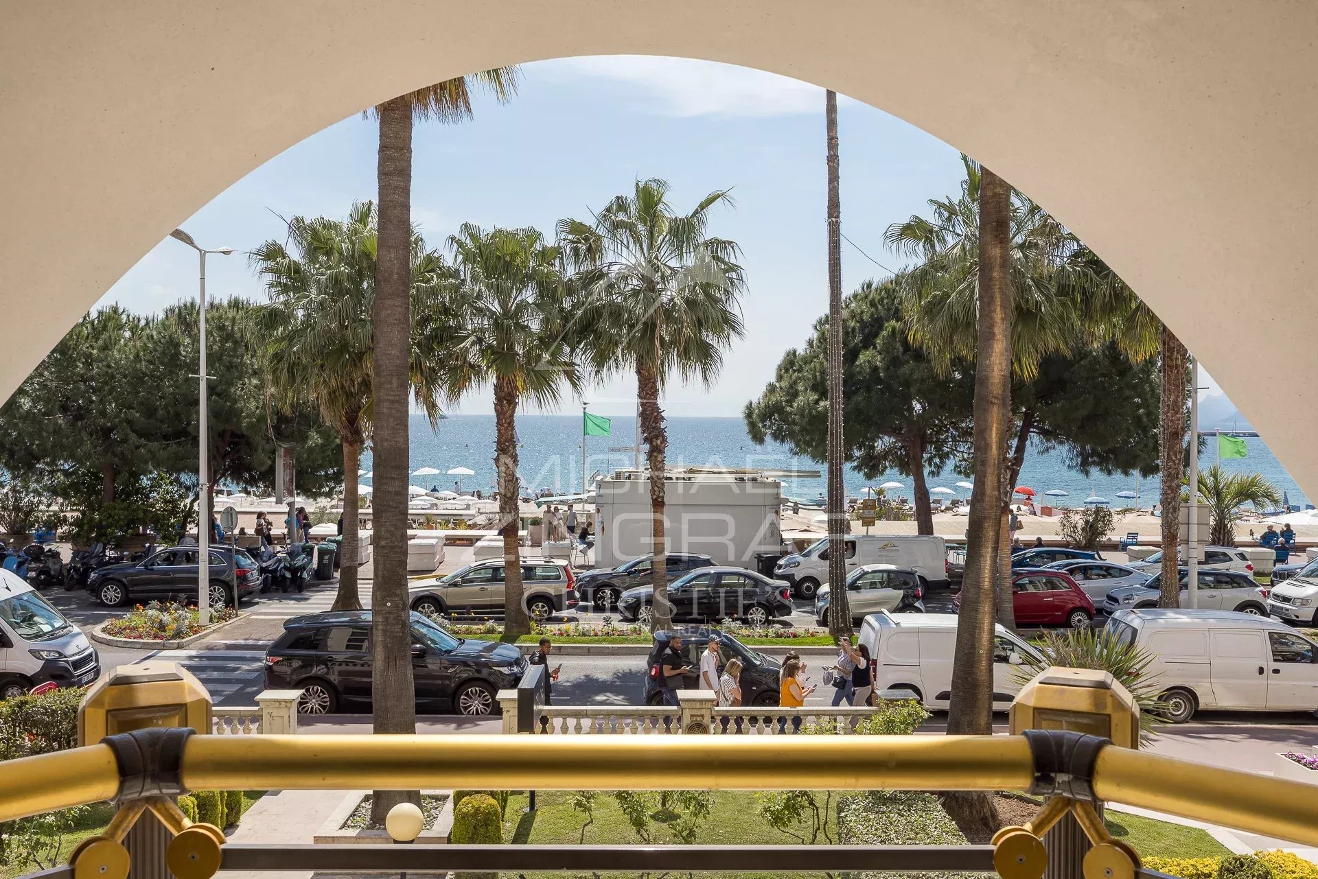Apartment with sea view in Cannes Panoramic sea view from an apartment on the Croisette in Cannes, with palm trees and cars below.