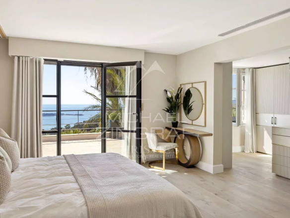 Chambre lumineuse avec vue sur la mer, décor moderne, fenêtres ouvertes sur l'extérieur.