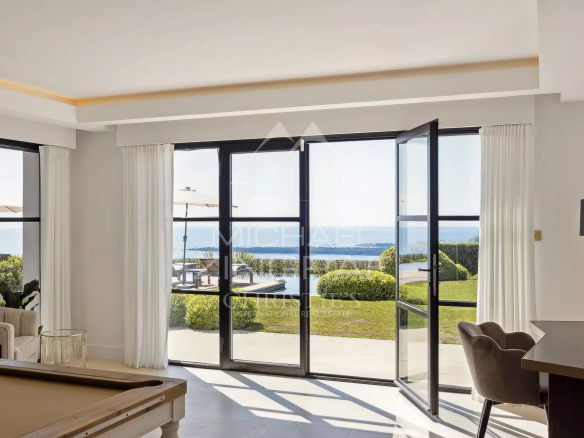 Intérieur d'une villa moderne avec vue panoramique sur la mer, grandes baies vitrées ouvertes.