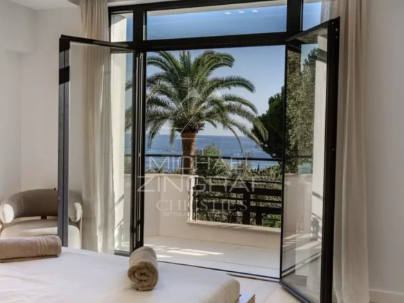 Vue depuis une chambre d'une villa neuve à Cap d'Antibes, avec des palmiers et la mer en arrière-plan.
