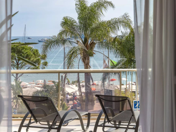Vue depuis une terrasse d'un appartement à Cannes, avec palmiers et mer en arrière-plan.