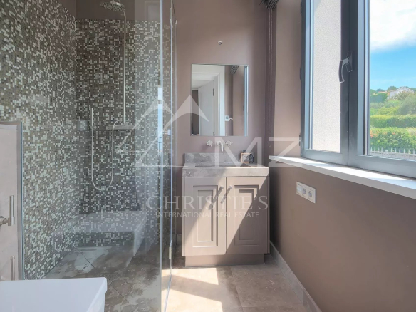 Salle de bains moderne avec douche et lavabo, murs carrelés en mosaïque, lumière naturelle à travers la fenêtre.