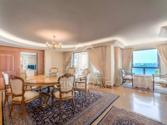 Intérieur d'un appartement de luxe à Cannes avec vue mer, salle à manger et fenêtres ouvertes sur la terrasse.