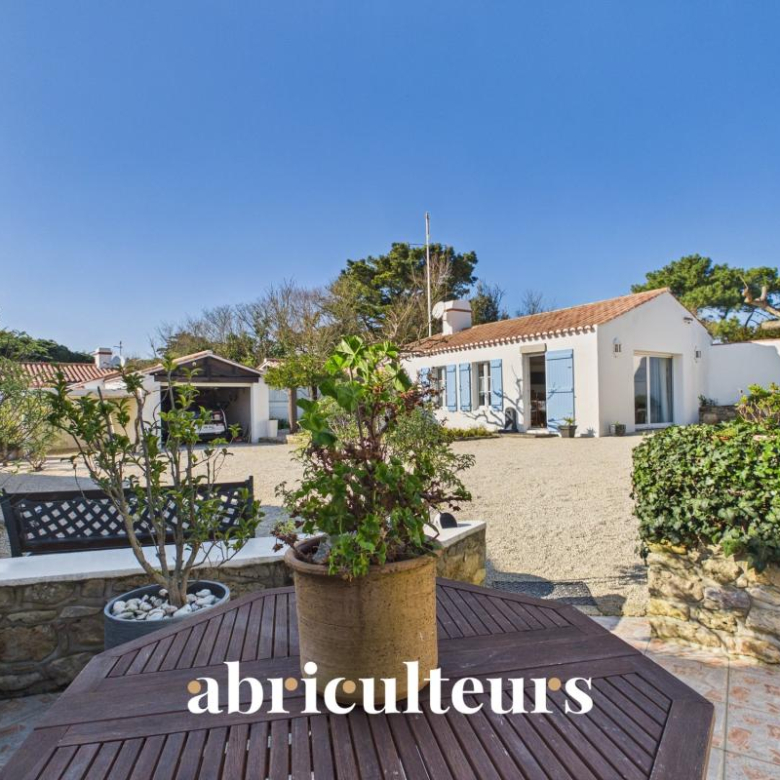 Sunny courtyard of a white Mediterranean villa with blue shutters and gravel yard, outdoor table in foreground.
