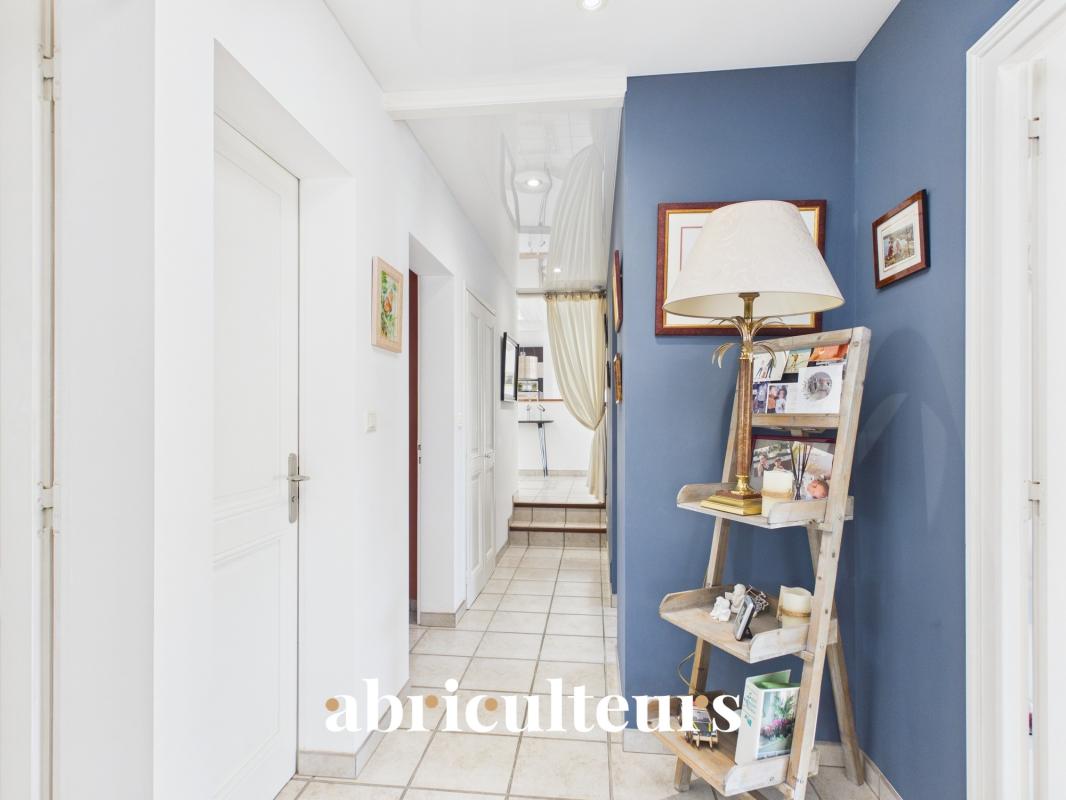 Cozy hallway with white walls and a blue accent wall, featuring a wooden ladder shelf holding a lamp, photos, and small decor items.