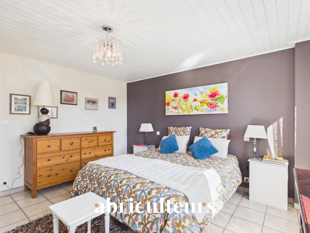 Bedroom with purple accent wall, queen bed in floral bedding and blue pillows, two white nightstands, lamps, and a crystal chandelier.