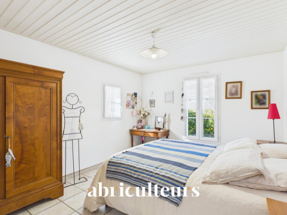 Bright bedroom with a wooden armoire, a bed with striped bedding, and a vanity table by a window.