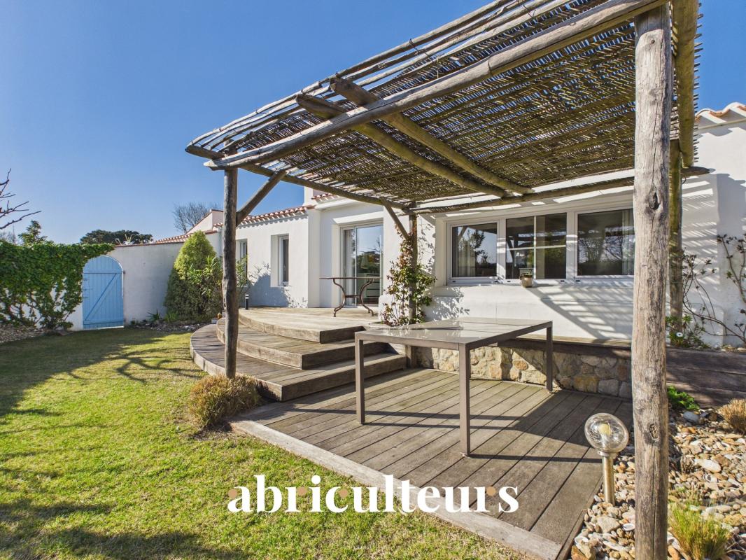 Backyard patio with a wooden deck and rustic pergola attached to a white house on a sunny day.