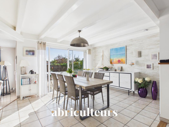 Bright open dining room with a wooden table, eight wicker chairs, and sliding glass doors to a sunny garden exterior, plus a modern sideboard and sailboat model.