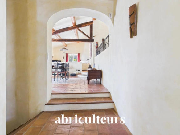 Interior with white walls and terracotta tile floors, archway opening to a rustic dining area with exposed wooden beams and chairs.