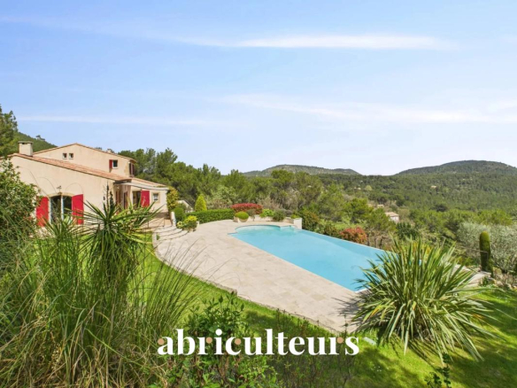 Countryside villa with beige walls and red shutters, a long rectangular pool, and lush landscaped grounds against rolling hills.