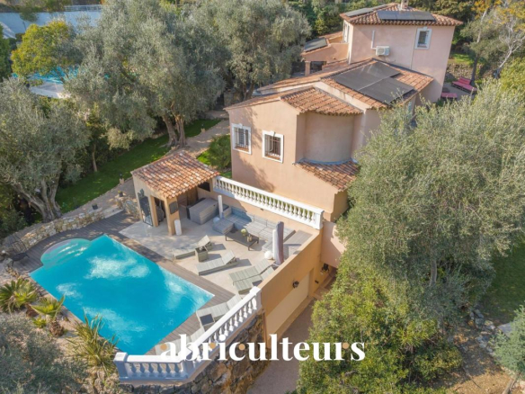 Aerial view of a beige Mediterranean villa with a terracotta roof, curved blue pool, and tiled terrace.
