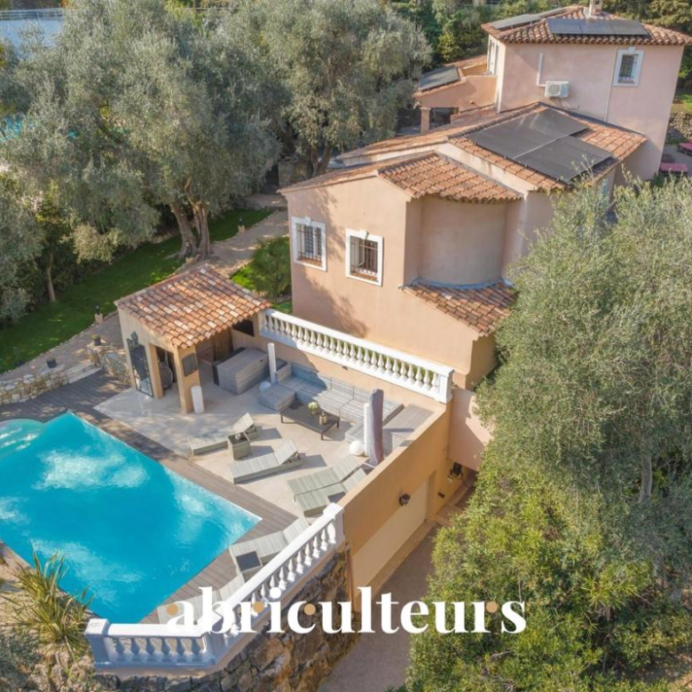 Aerial view of a beige Mediterranean villa with a terracotta roof, curved blue pool, and tiled terrace.