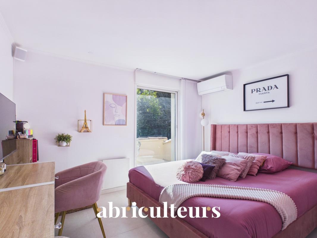 Pink bedroom with a tufted pink bed, plush pillows, a knit blanket, and a pink chair by a wooden desk; glass balcony door in the background.