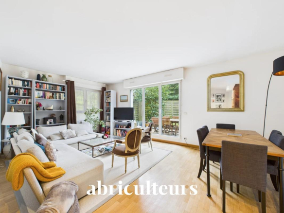 Bright open living room with a beige sectional, bookshelves, coffee table, and a dining area; sliding doors open to a garden patio on the right side.