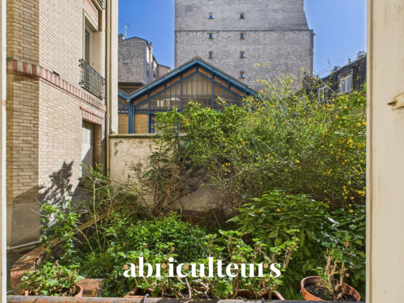 Urban courtyard garden with potted plants and a blue-framed glass conservatory, brick buildings nearby, and the word 'abliculteurs' at the bottom.