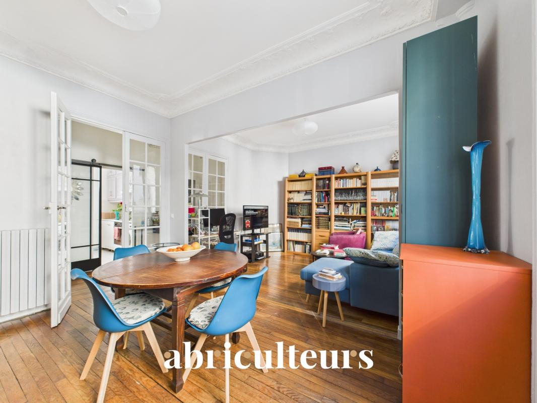 Open living and dining area with a round wooden table, blue chairs, bookshelves, and a blue sofa; watermark 'abriculturists'.