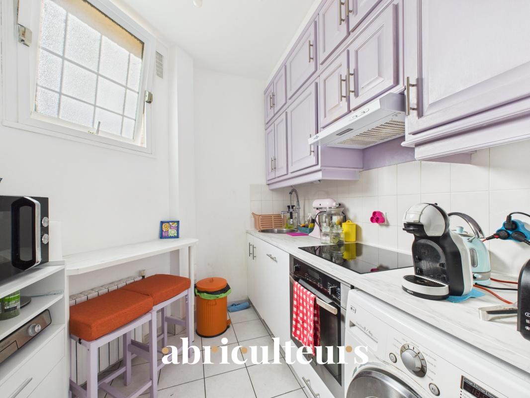 Cozy galley kitchen with lilac cabinets, white countertops, and orange bar stools by a small table under a window.