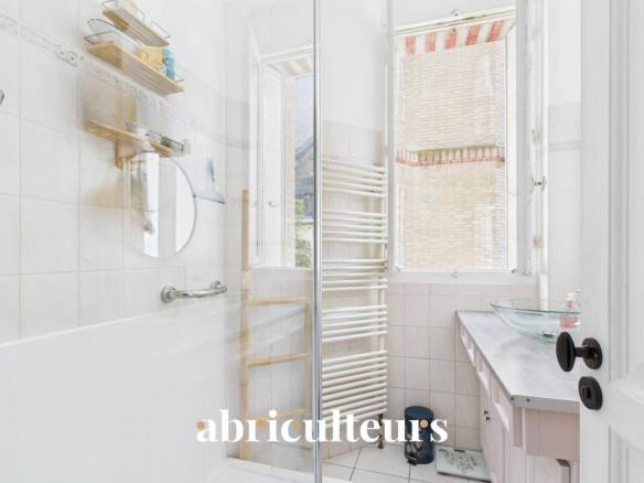 Bright bathroom with a glass shower enclosure, white tiled walls, and a wall-mounted towel warmer near a window.