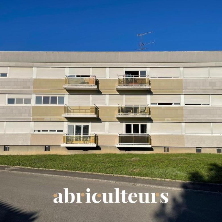 Four-story apartment building with beige-gray panels and small balconies against a blue sky; the word 'abriculteurs' appears along the street in the foreground.