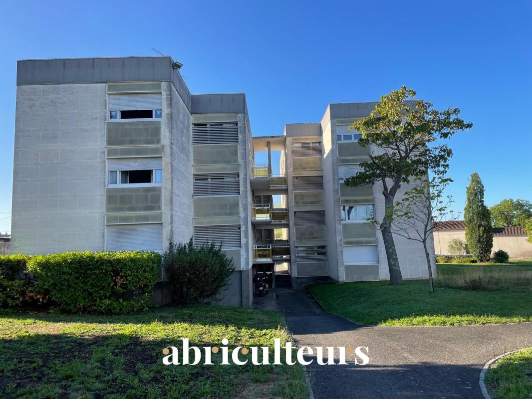 Three-story concrete apartment building with a central open stairwell, greenery, and a blue sky above.