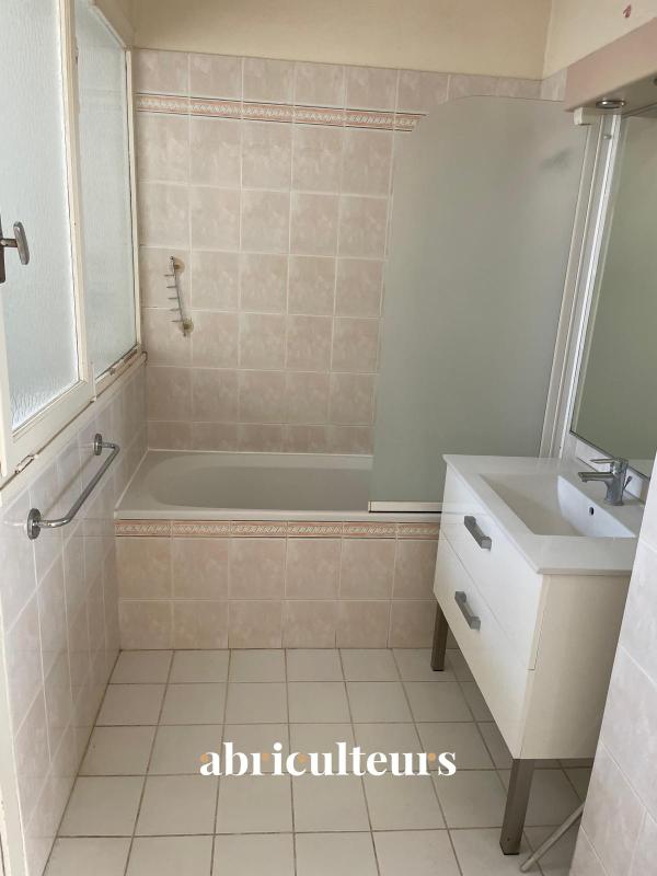 Bathroom with a built-in bathtub, frosted glass shower screen, white vanity, and beige tiled walls/flooring with a window on the left.