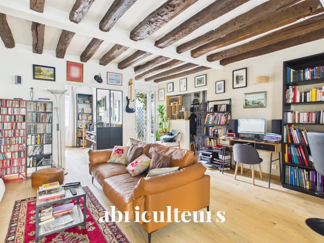 Living room of a two-room apartment in Paris 11 with exposed beams and a bookcase.