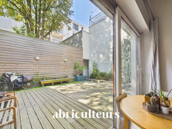 Wooden terrace with chairs and a green space, seen from inside a duplex in Paris 20th arrondissement.