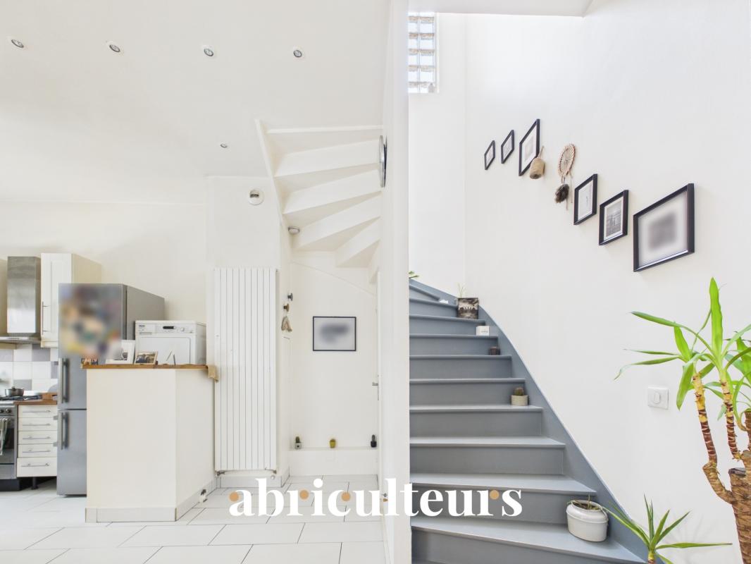 Interior of a duplex in Paris 20th with living room, open kitchen and staircase.