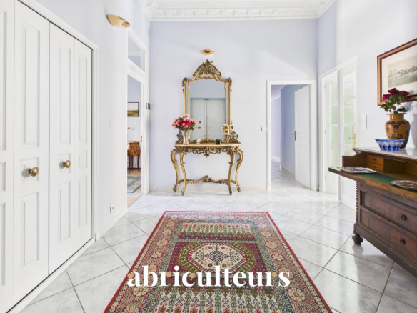 Entrée d'un appartement rénové avec un tapis coloré et un miroir doré, murs clairs et carrelage.