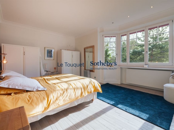 Chambre spacieuse avec lit, moquette bleue et fenêtres donnant sur un jardin à Le Touquet.