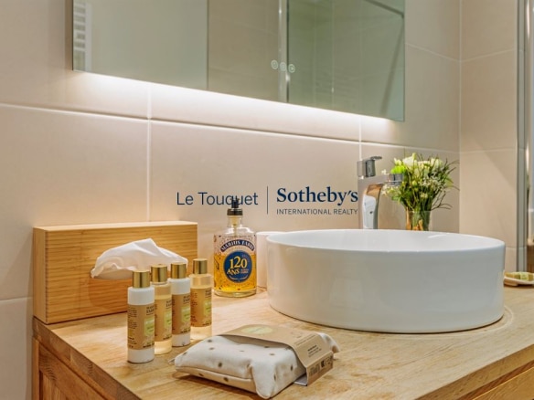 Salle de bain moderne avec lavabo rond et produits de soin sur un meuble en bois.
