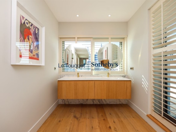 Modern bathroom with double wooden sink and round mirror, decorated with artwork.