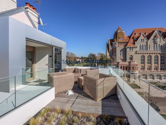 Terrasse d'une villa contemporaine avec fauteuils en osier, vue sur un bâtiment emblématique à Le Touquet-Paris-Plage.