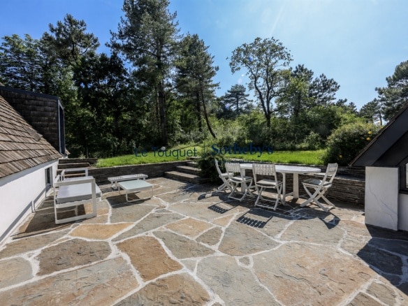 Stone terrace with garden furniture, surrounded by maritime pines and dunes in Le Touquet.
